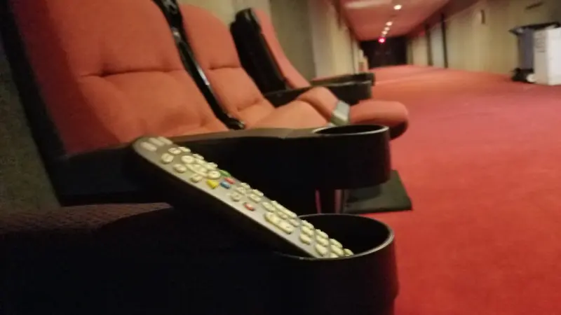 Poltronas vermelhas de cinema com um controle remoto apoiado no braço da poltrona.