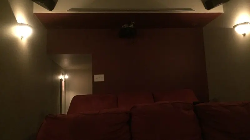Sala de cinema em casa com poltronas vermelhas e luminárias nas paredes.